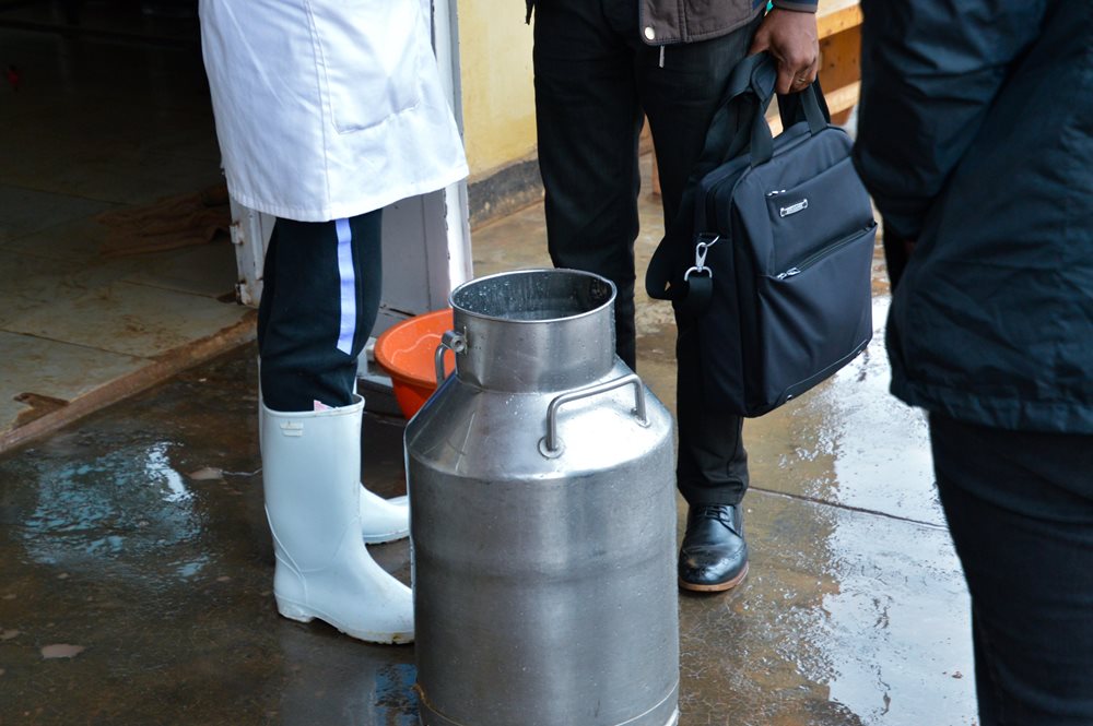 BTK cooperative members stand in rubber boots near milk jug at their collection facility