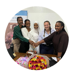 Morgan and four interns slice into a celebratory cake. Flowers and gifts are in the foreground.